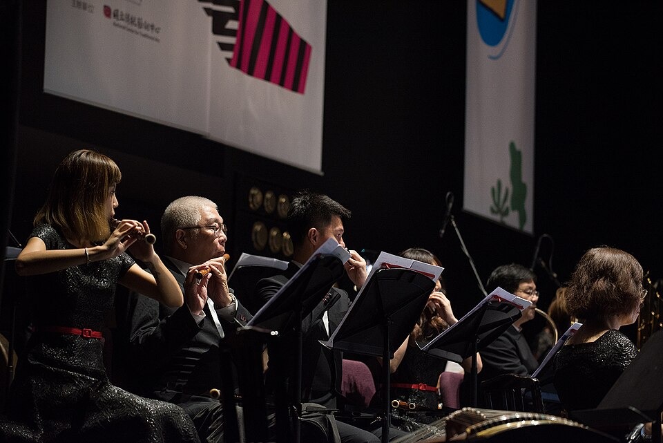 A row of musicians in a Chinese orchestra hold dizi flutes sideways to their lips