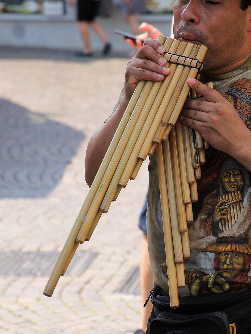 A musician holds bamboo siku panpipes of different lengths to his lips