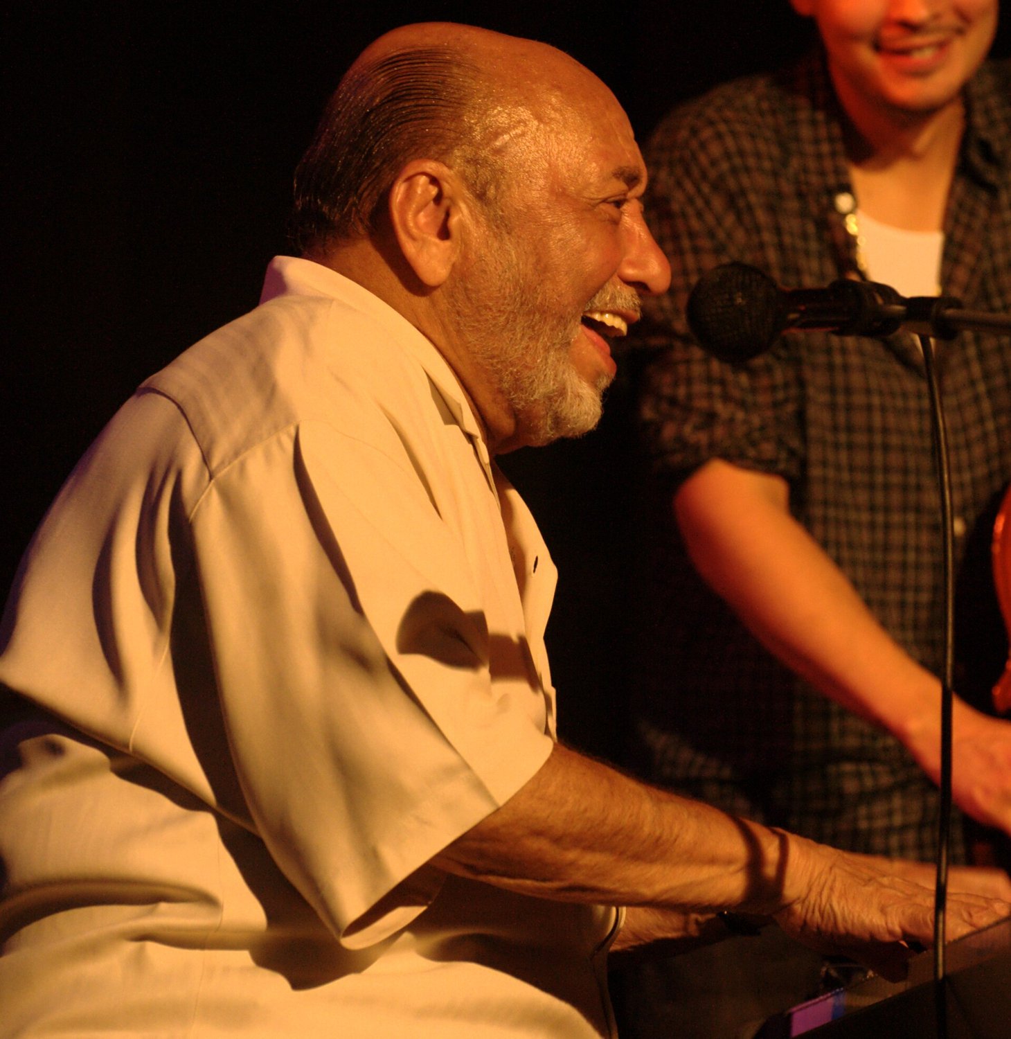 Eddie Palmieri laughing at the keyboard beside a microphone