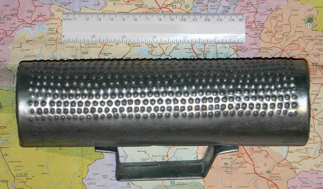 A metal güira: a cylinder covered in small raised bumps with a handle underneath, next to a 15-centimeter ruler