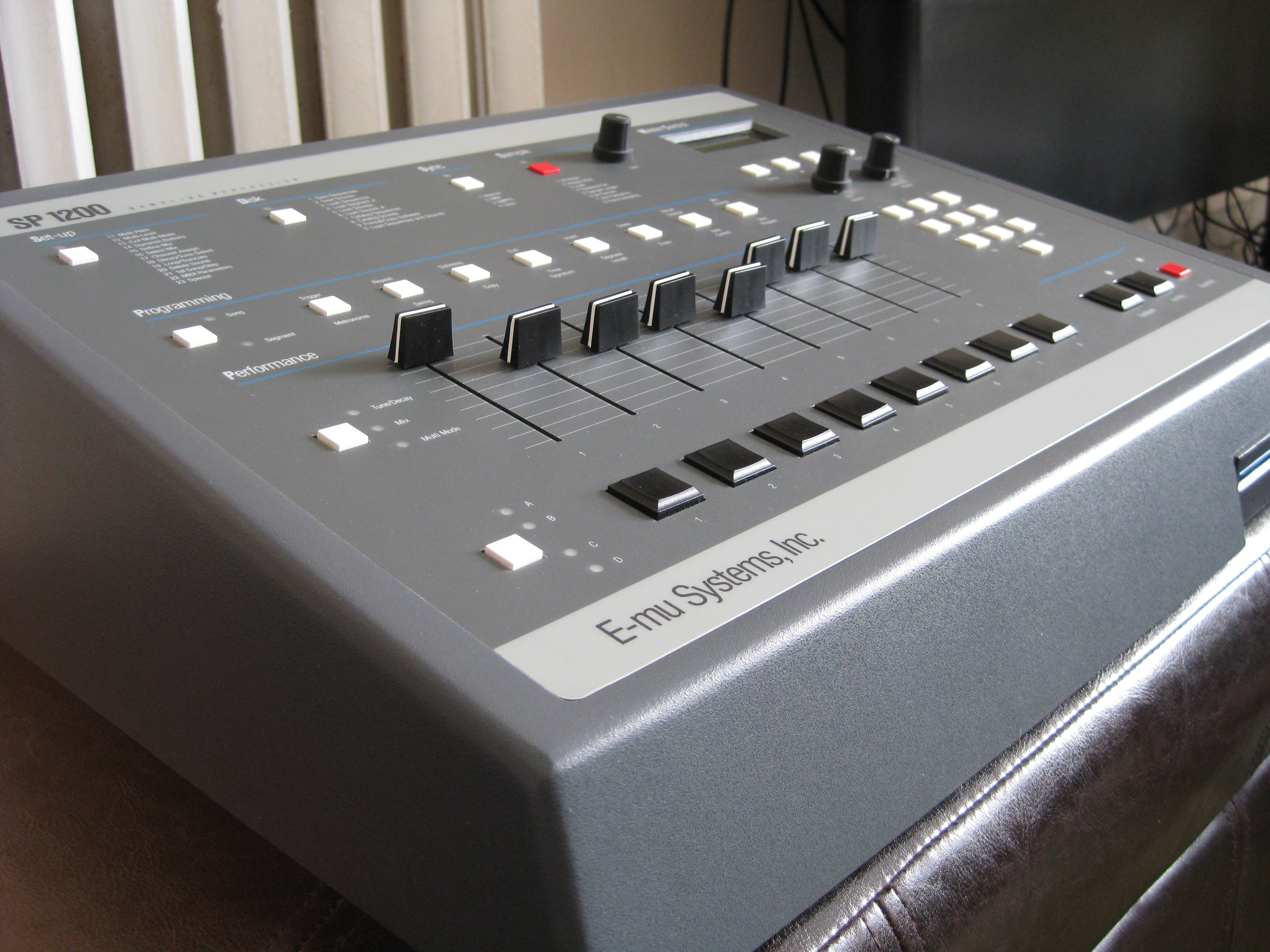 An E-mu SP-1200 sampling drum machine: rows of white buttons, eight black sliders and eight black pads