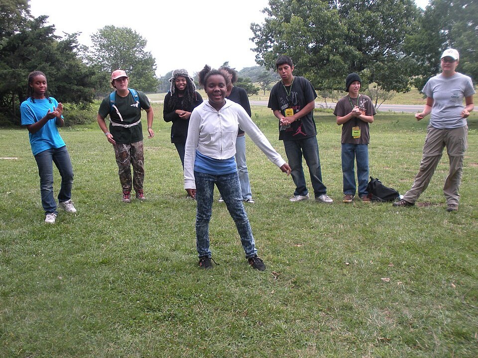 Teenagers in a circle outdoors while one steps into the middle