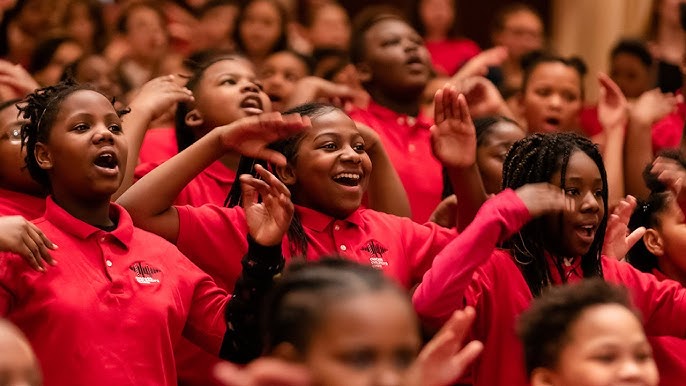 Children's choir in red shirts singing together with hands raised